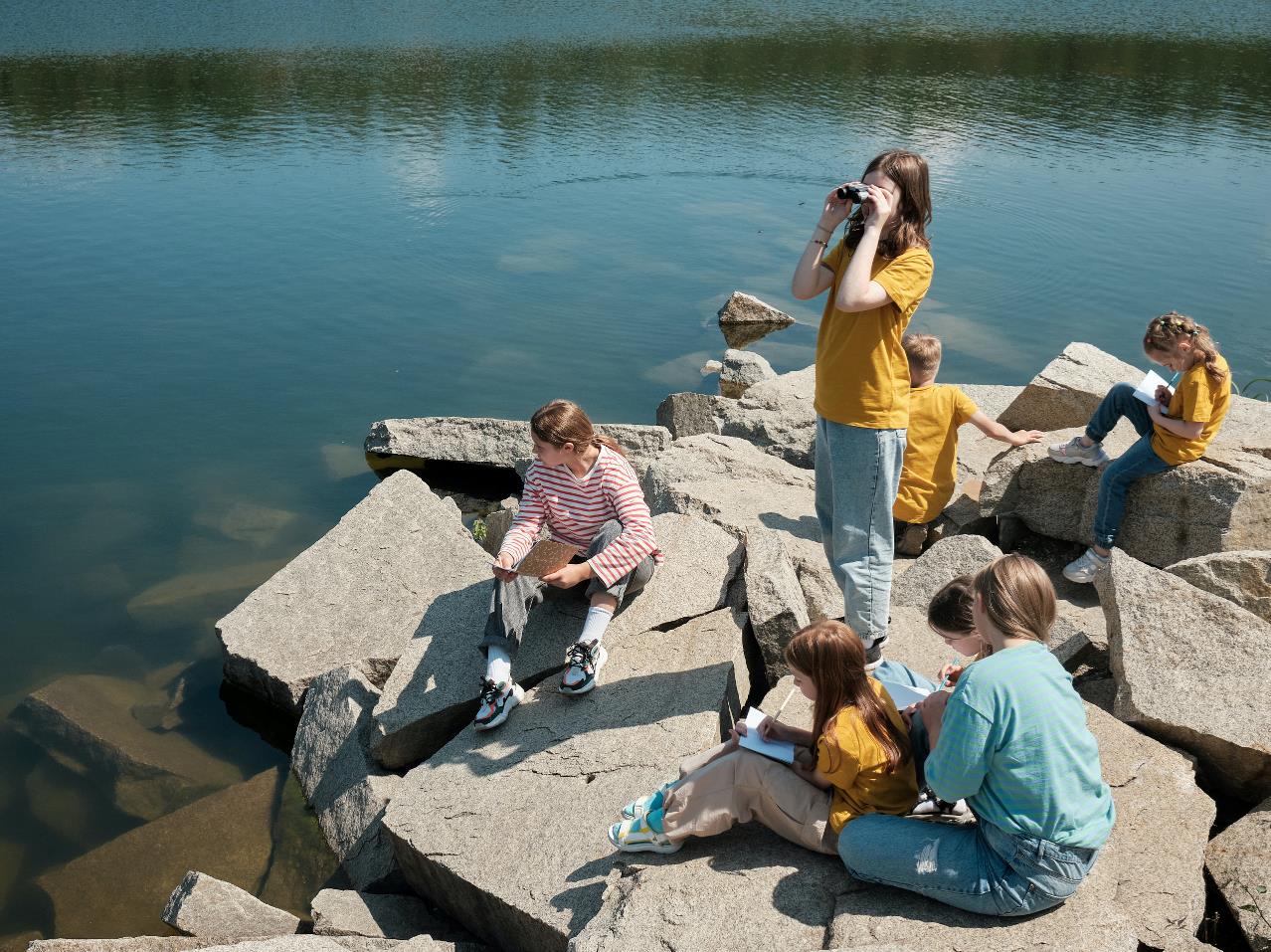 En gruppe børn sidder på sten og kigger ud over vandet